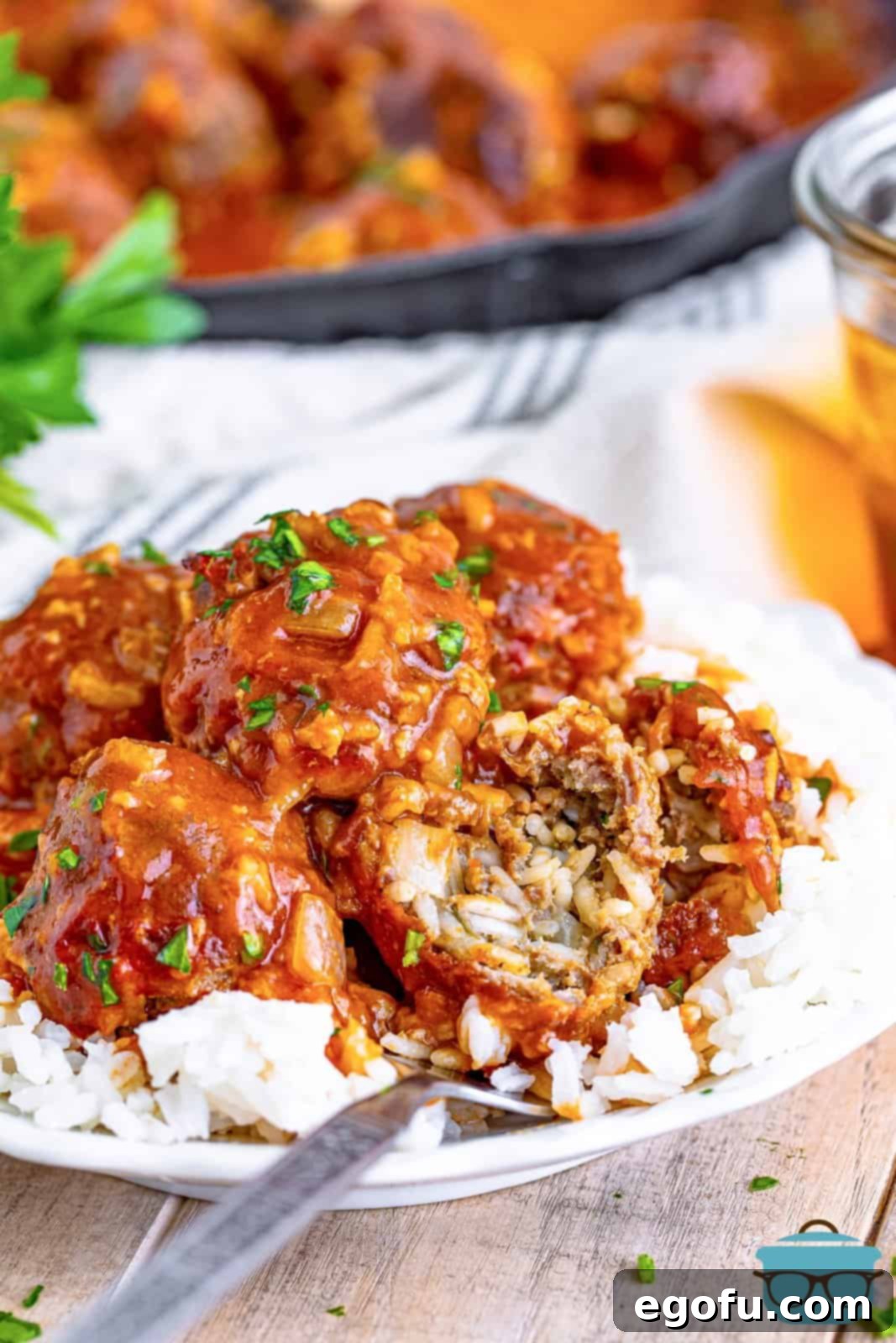 A plate of rice with porcupine meatballs on top, one with a bite taken out, showcasing the tender rice inside.