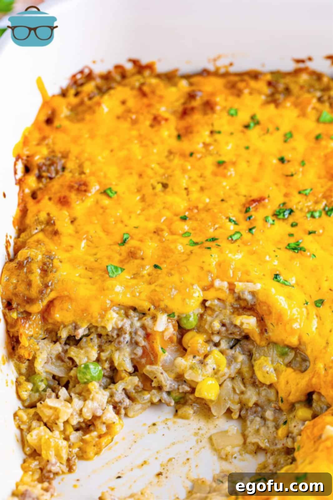 Golden Cheesy Beef and Rice Bake 2 A baking dish with a cheesy ground beef and rice casserole with a scoop taken out of it, showing layers of beef, rice, and cheese.
