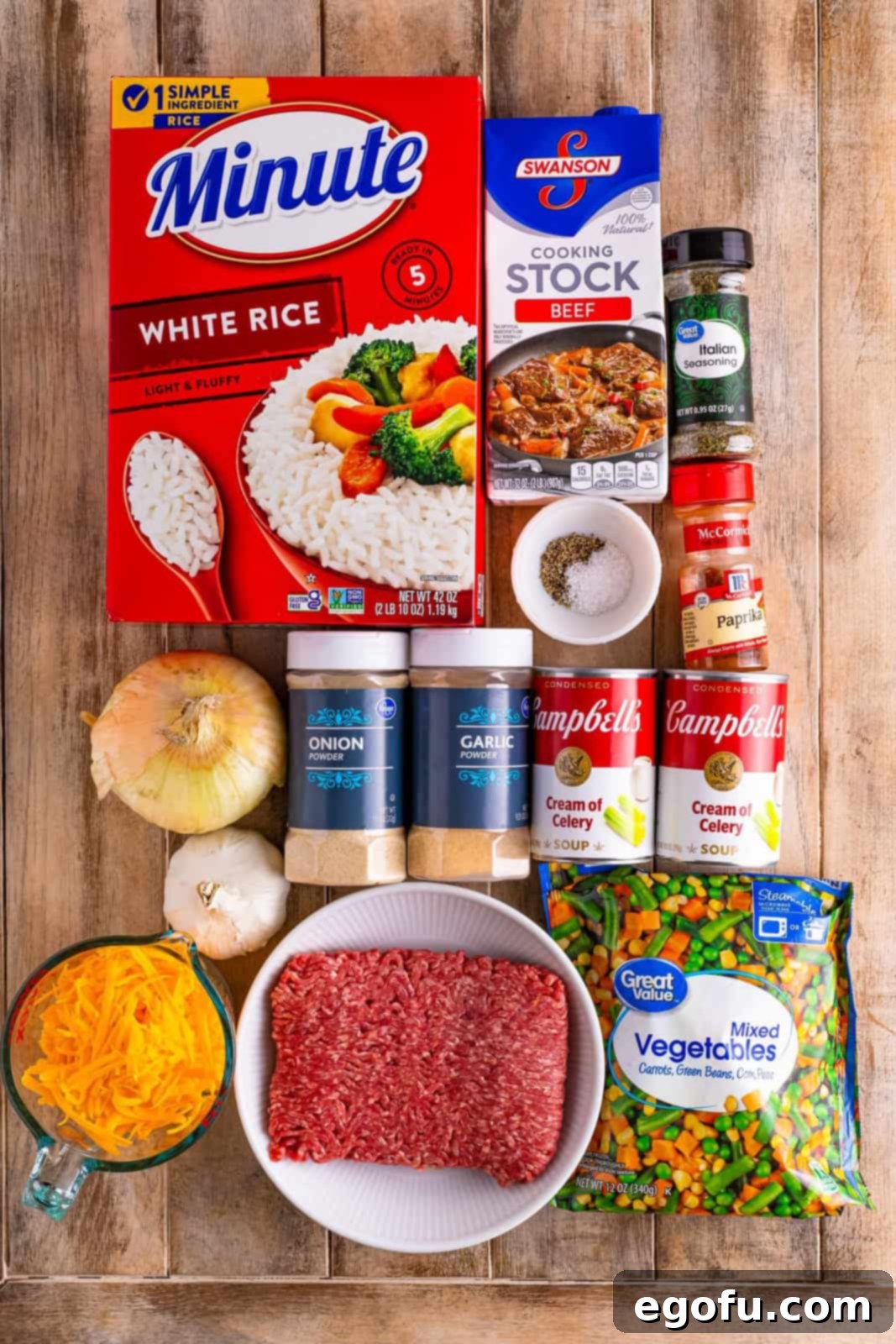 Golden Cheesy Beef and Rice Bake 4 Ground beef, sweet onion, garlic cloves, cream of celery soup, beef stock, garlic powder, onion powder, Italian seasoning, sweet paprika, kosher salt, black pepper, instant rice, frozen mixed vegetables, shredded sharp cheddar cheese, and fresh chopped parsley, all laid out on a table.