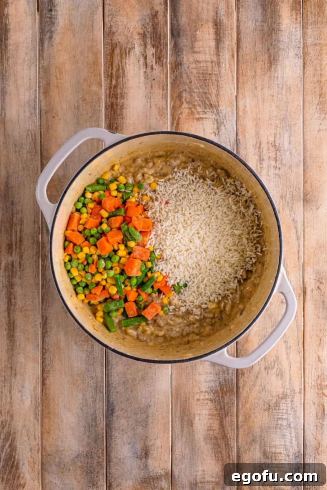 Golden Cheesy Beef and Rice Bake 7 A dutch oven filled with the complete casserole mixture including ground beef, condensed soup, spices, onion, garlic, frozen mixed veggies, and instant rice, all ready for transfer.