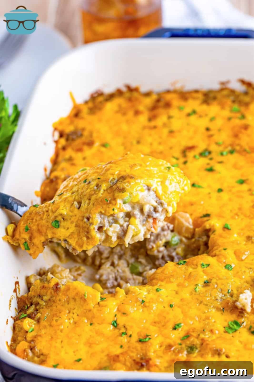 Golden Cheesy Beef and Rice Bake 10 A serving utensil holding a generous scoop of cheesy ground beef and rice casserole, ready to be placed on a plate.