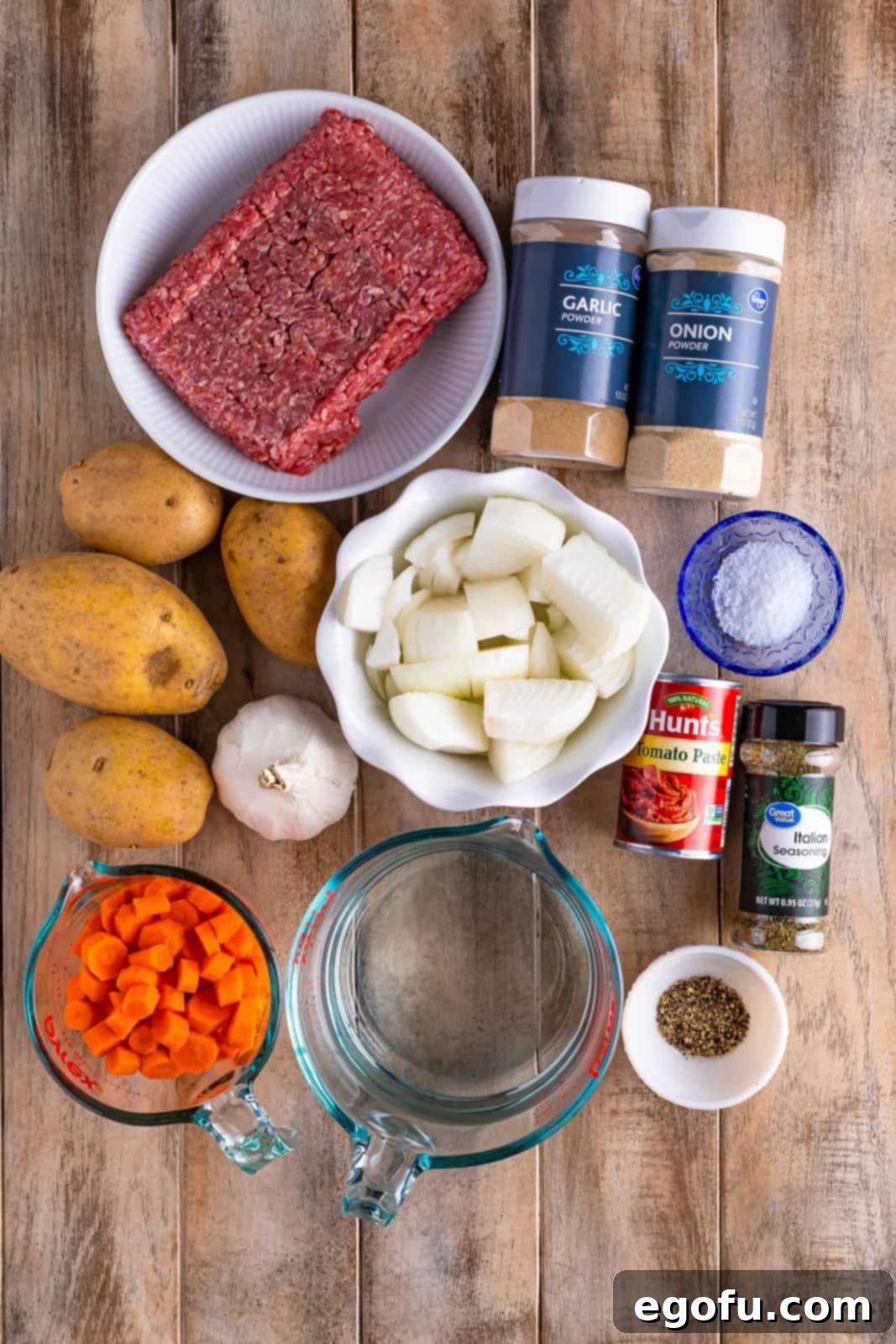 Slow Cooker Humble Stew 4 Individual ingredients for Slow Cooker Poor Man's Stew laid out: Ground beef, yukon gold potatoes, diced carrot, onion, garlic, water, tomato paste, Italian seasoning, kosher salt, garlic powder, onion powder, and black pepper.