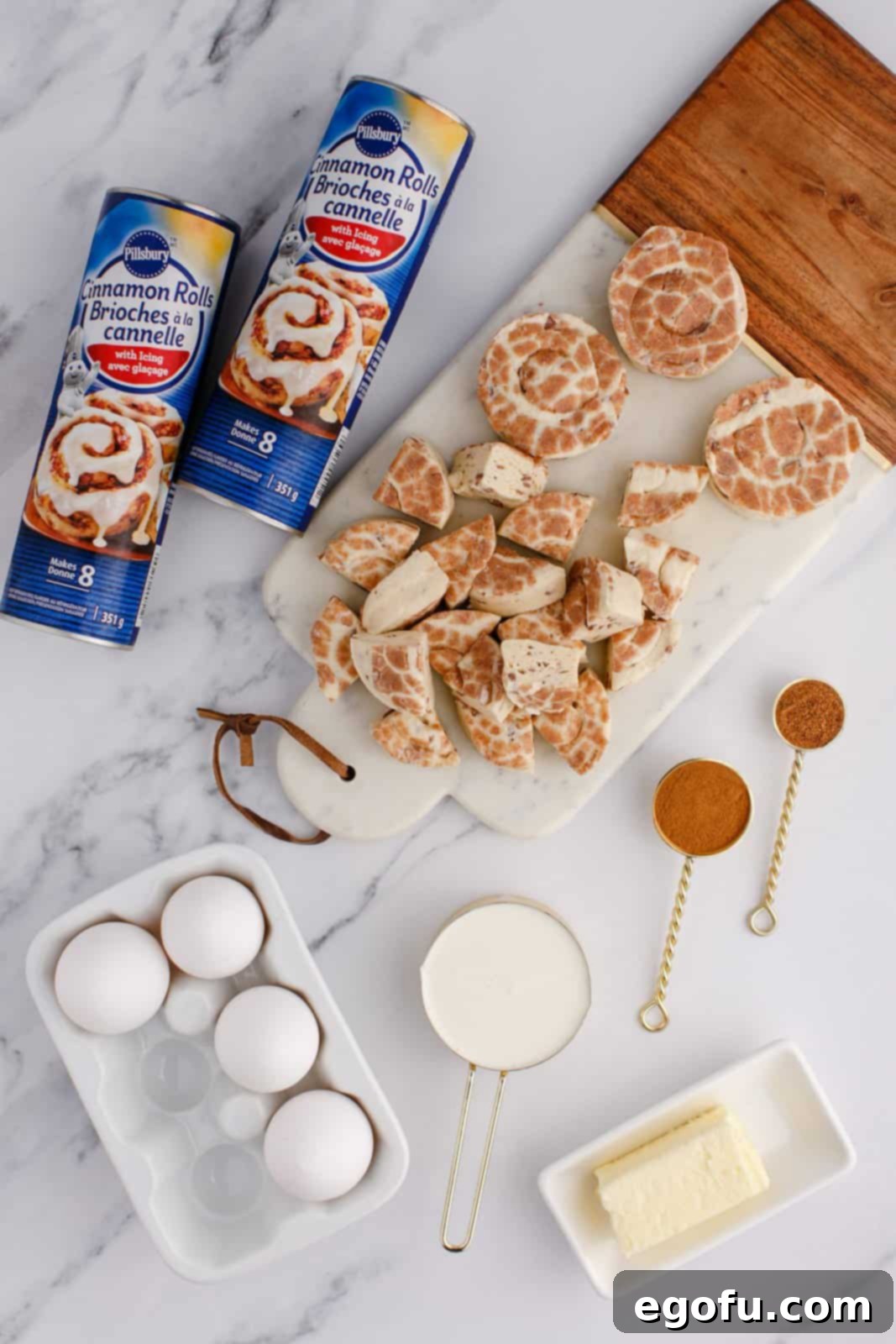Pull-Apart Cinnamon Delight 4 Two tubes of cinnamon rolls, eggs, ground nutmeg, heavy whipping cream, and ground cinnamon on a wooden surface, ready for baking.