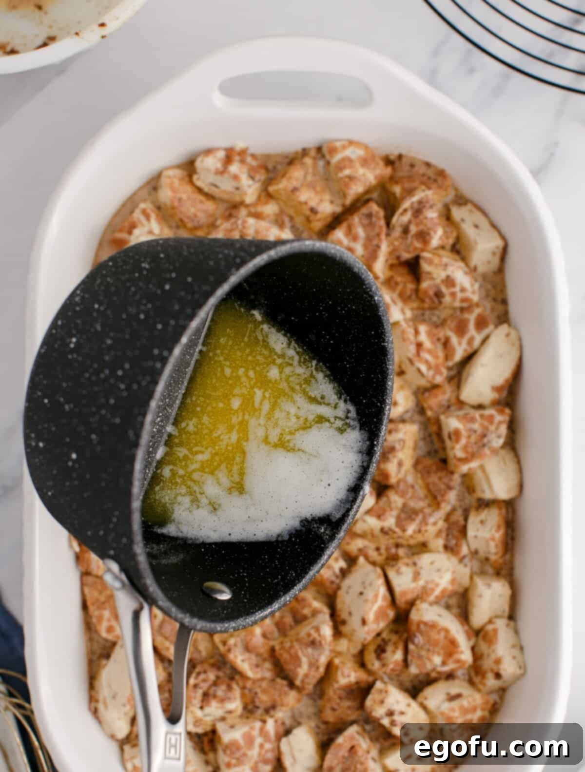 Pull-Apart Cinnamon Delight 7 A pot of melted butter being poured over a casserole dish filled with cut up cinnamon rolls and custard mixture.