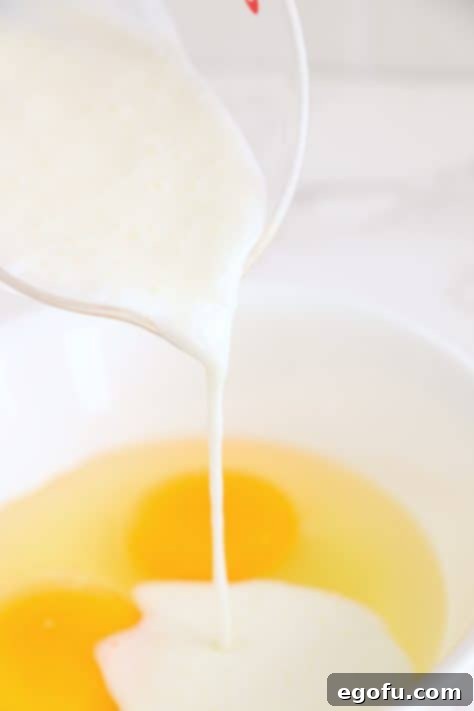 A mixing bowl with eggs and buttermilk being poured in.
