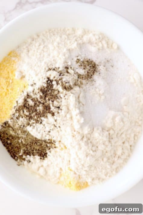 A mixing bowl with flour, garlic powder, cornmeal, parmesan cheese, salt and pepper.