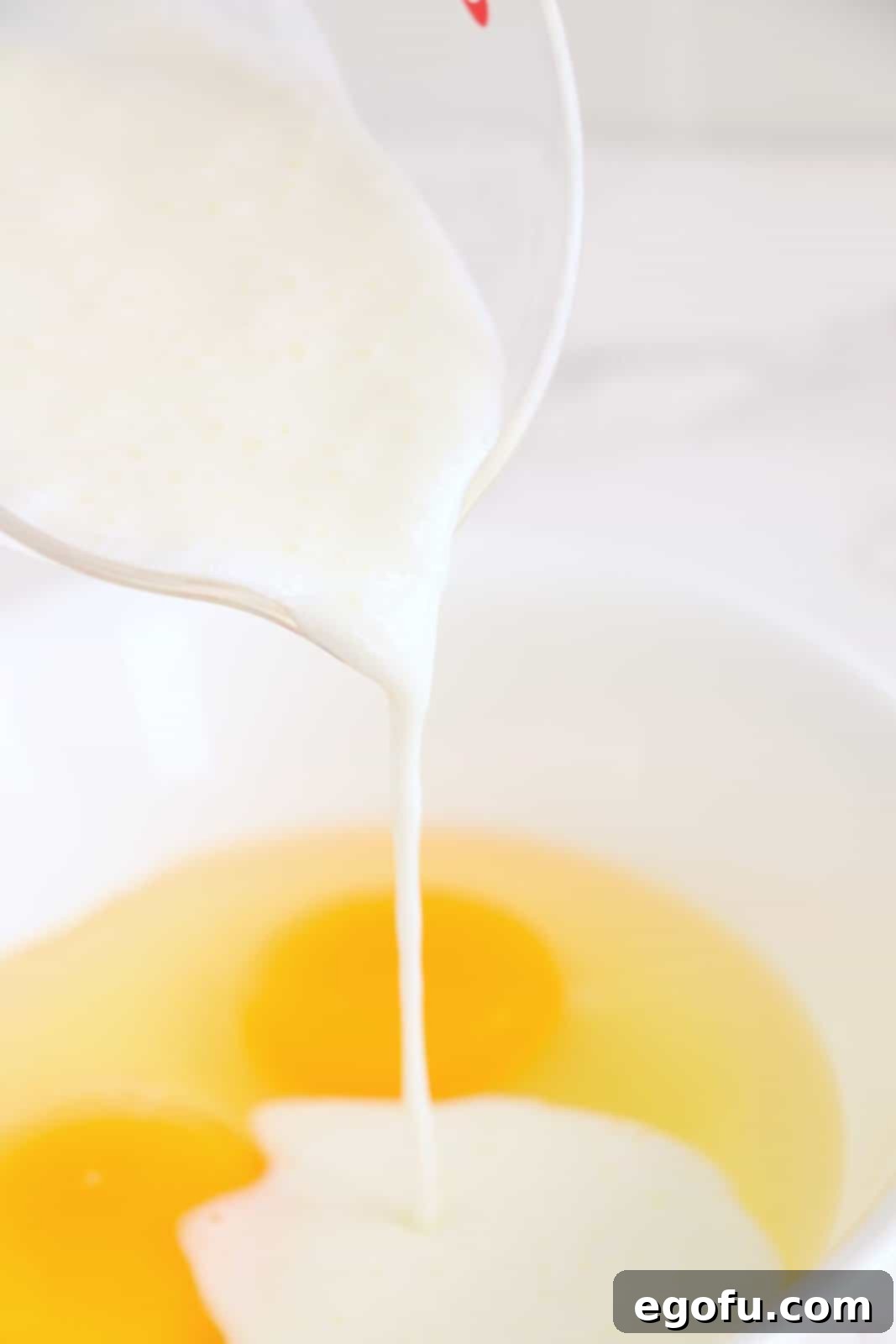 A mixing bowl with eggs and buttermilk being poured in.