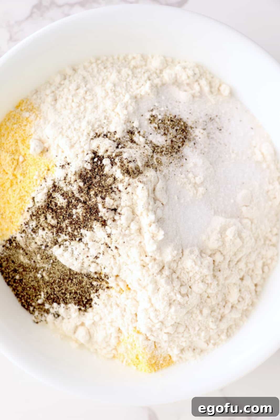 A mixing bowl with flour, garlic powder, cornmeal, parmesan cheese, salt and pepper.