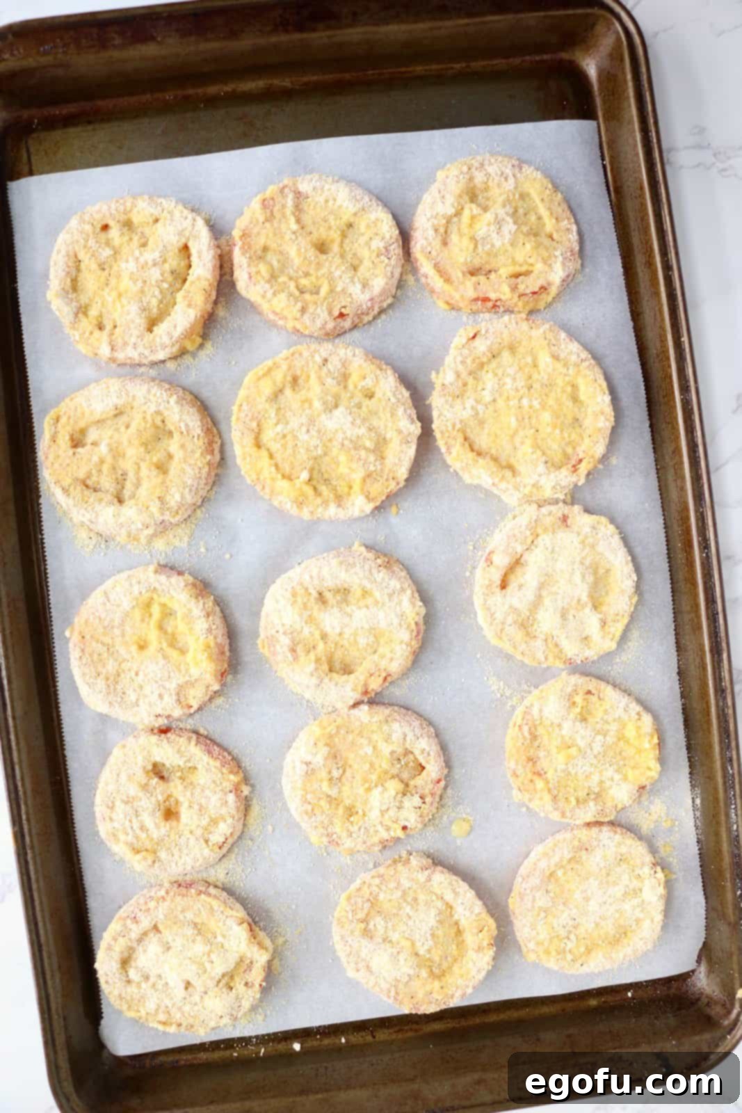 A baking sheet lined with parchment paper and breaded tomatoes on top.