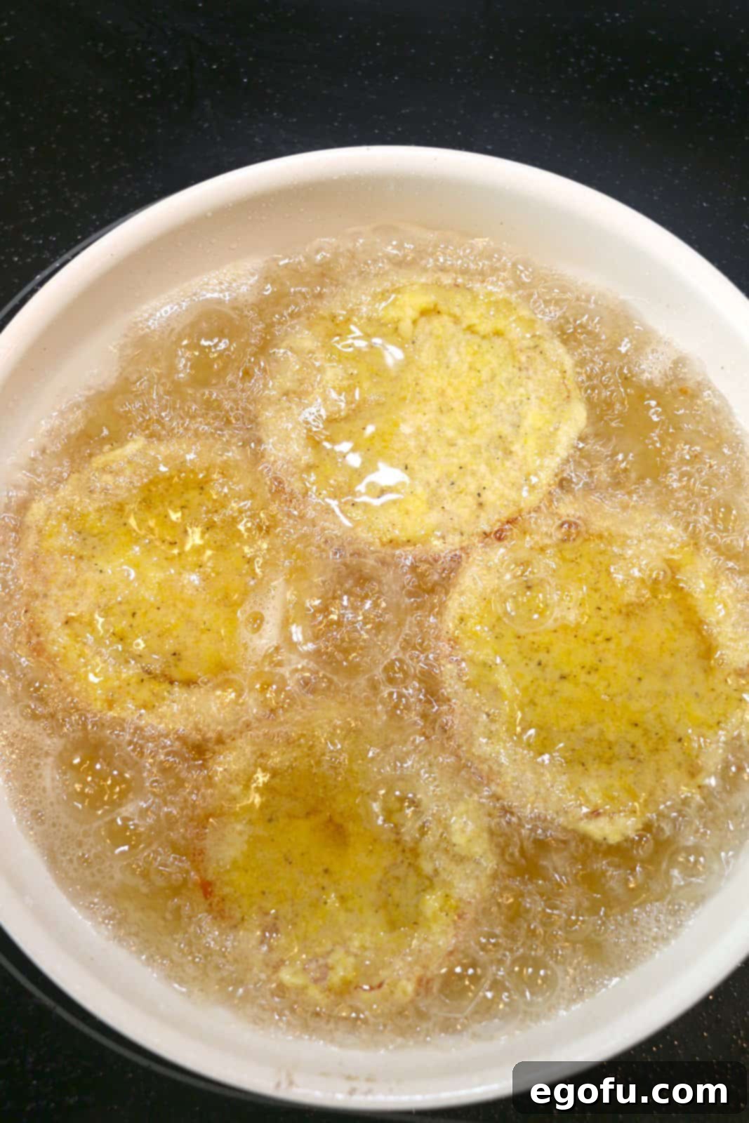 Breaded tomatoes in a skillet with frying oil.