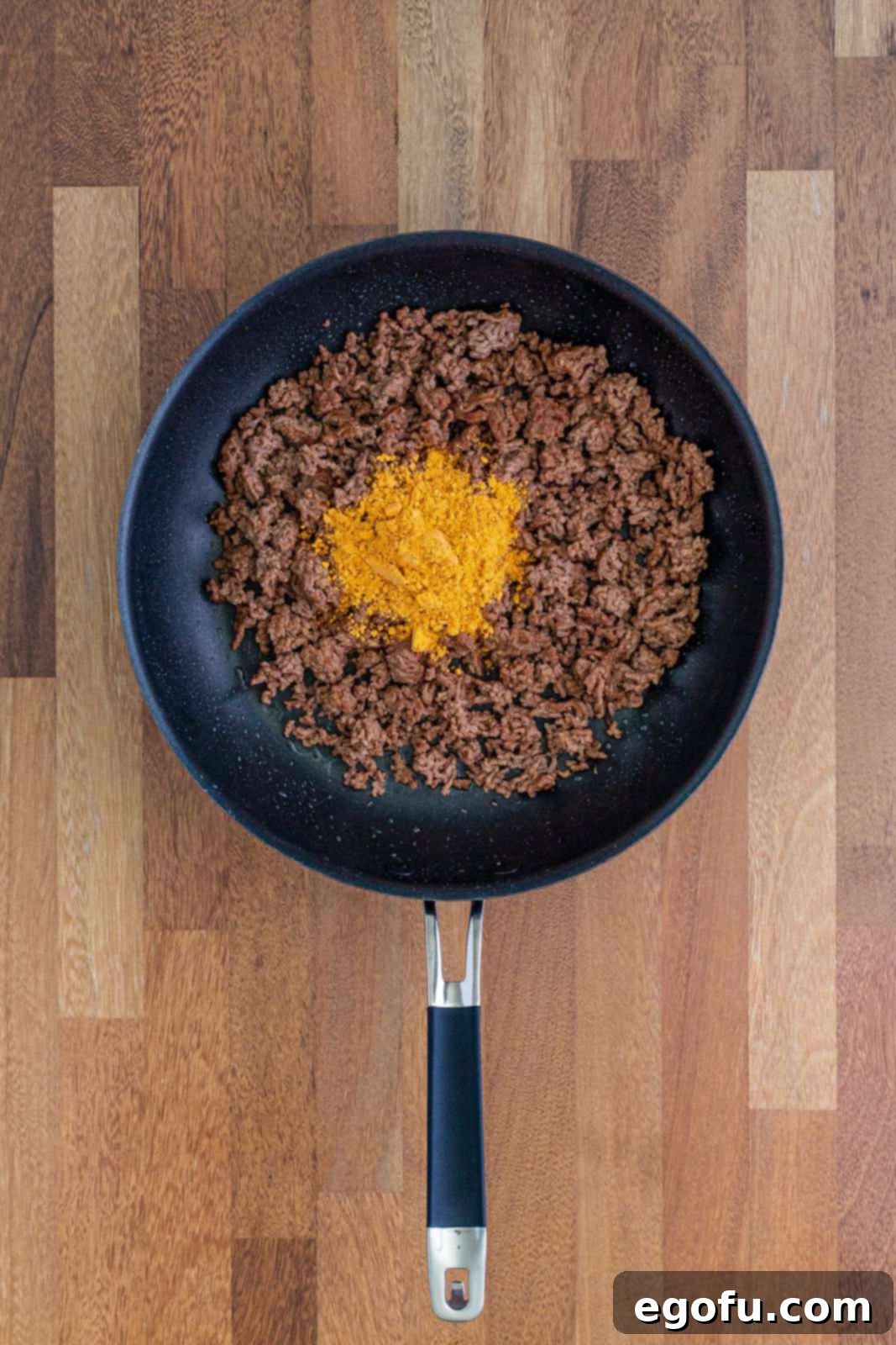 Ground beef with taco seasoning in skillet, being stirred to combine flavors.