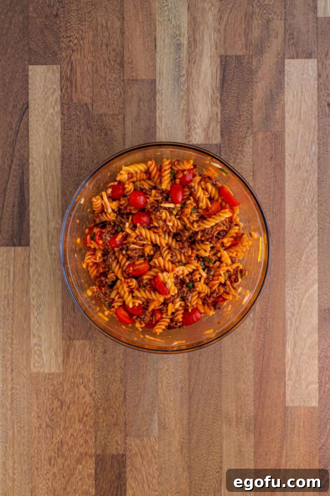 A mixed up bowl of most of the ingredients for Taco Pasta Salad, covered and chilling.