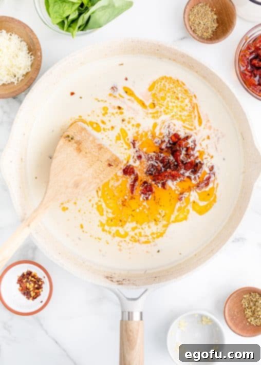 Proposal Chicken 14 A pan of cream sauce with sun-dried tomatoes being stirred in.