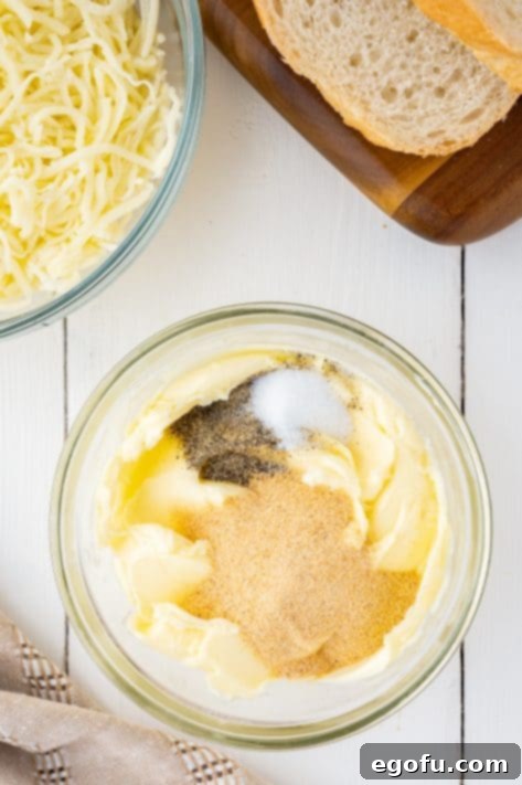A mixing bowl with softened butter, garlic powder, salt and pepper.