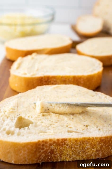 A knife spreading garlic butter on a slice of bread.