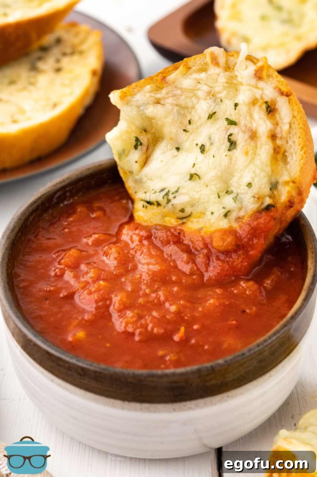 A piece of garlic bread being dipped in a bowl of marinara sauce.