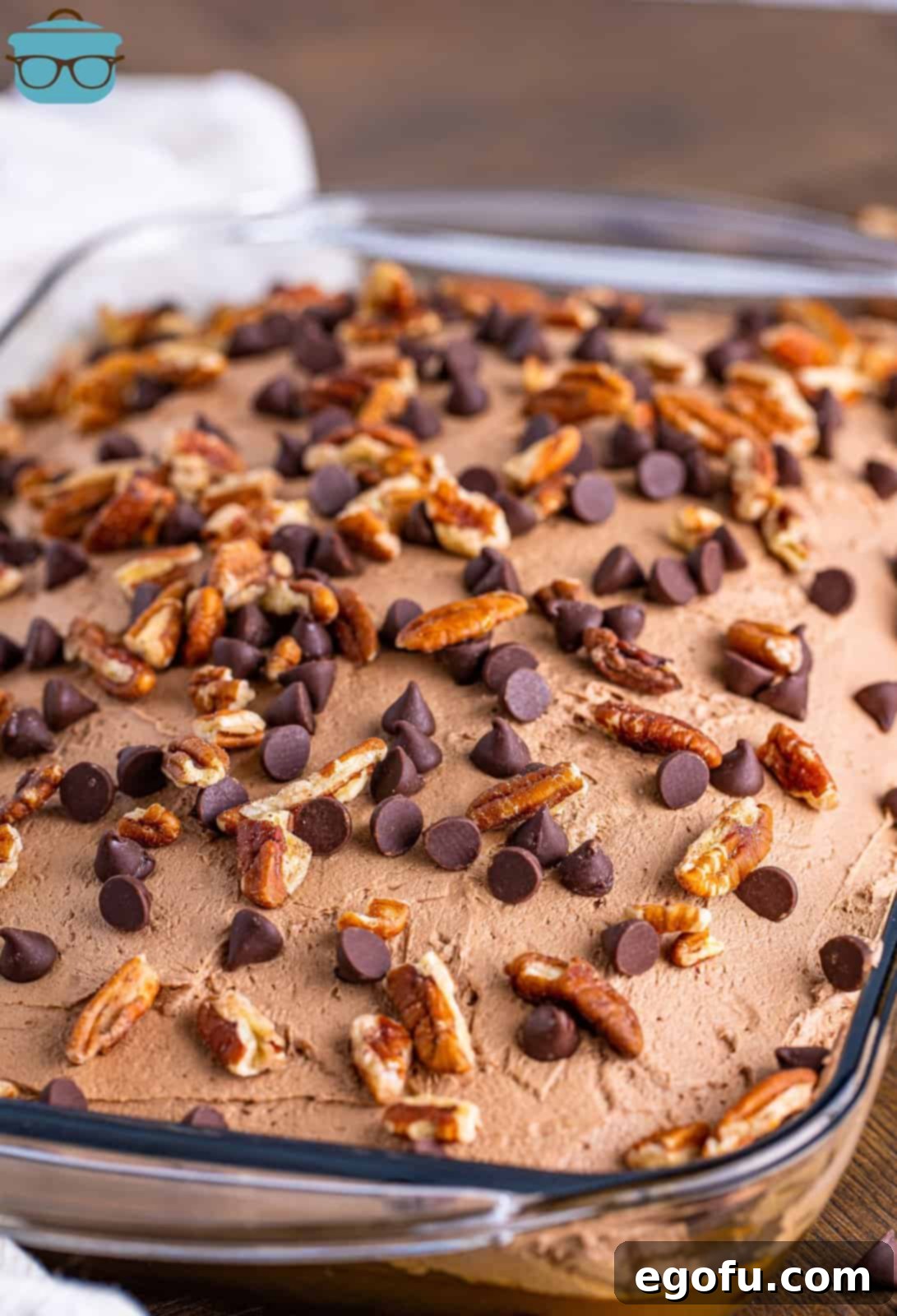 A baking dish with turtle poke cake and chopped nuts and chocolate chips on top.