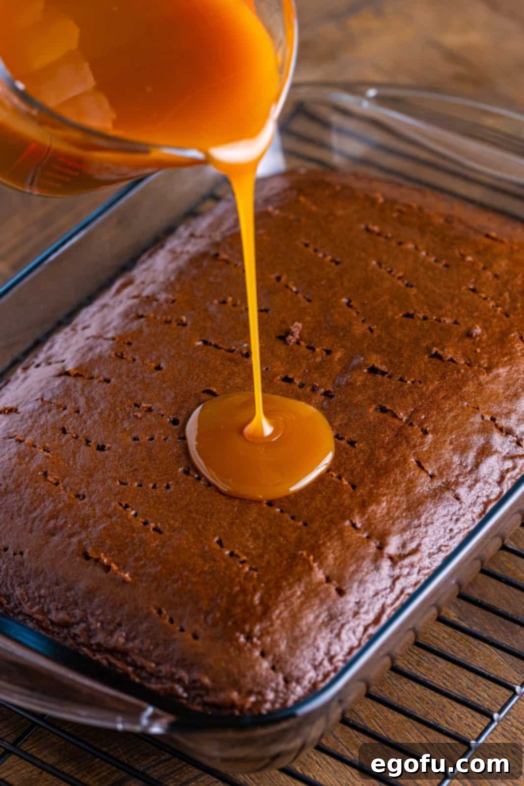 Caramel topping being poured on a chocolate cake with fork holes.