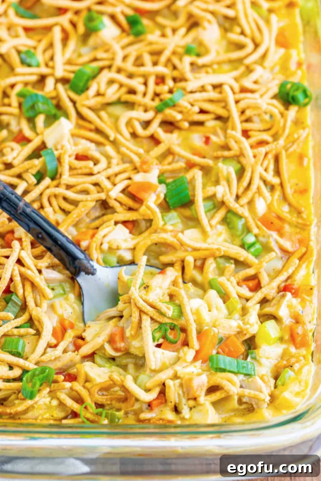 A baking dish with chicken chow mein casserole and a utensil in it. 