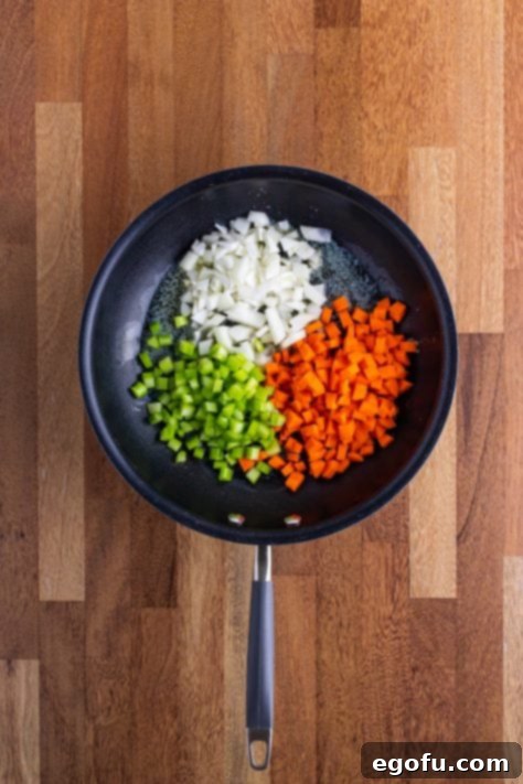 A skillet with onion, carrots and celery in it.