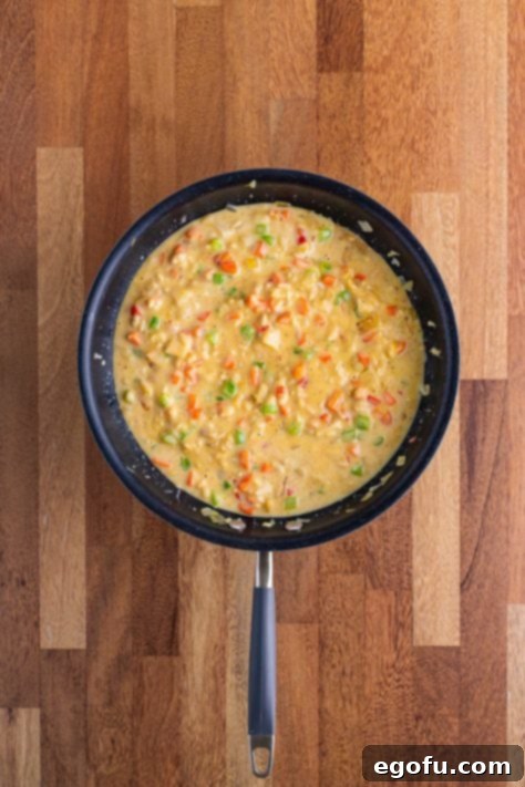 A skillet with carrots, celery, onion, butter, water chestnuts, cream of chicken soup, chicken and rice soup, milk, pepper and soy sauce.