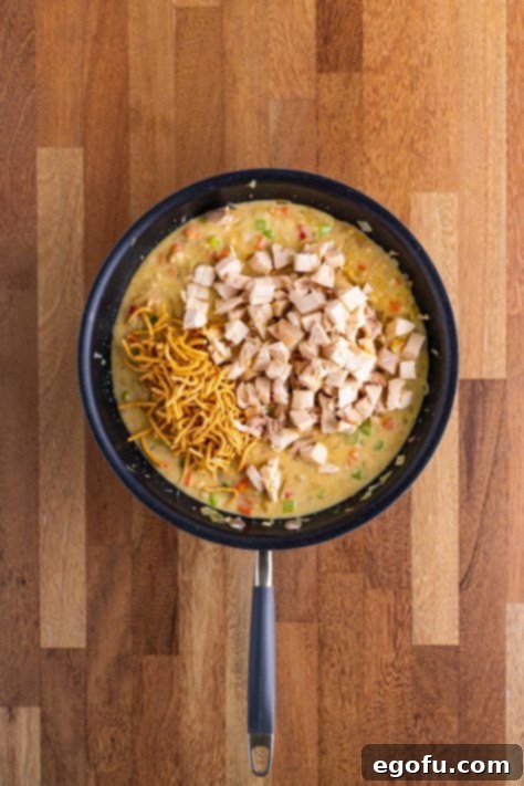 A skillet with ingredients cooking down and chicken and some chow mein noodles on top.