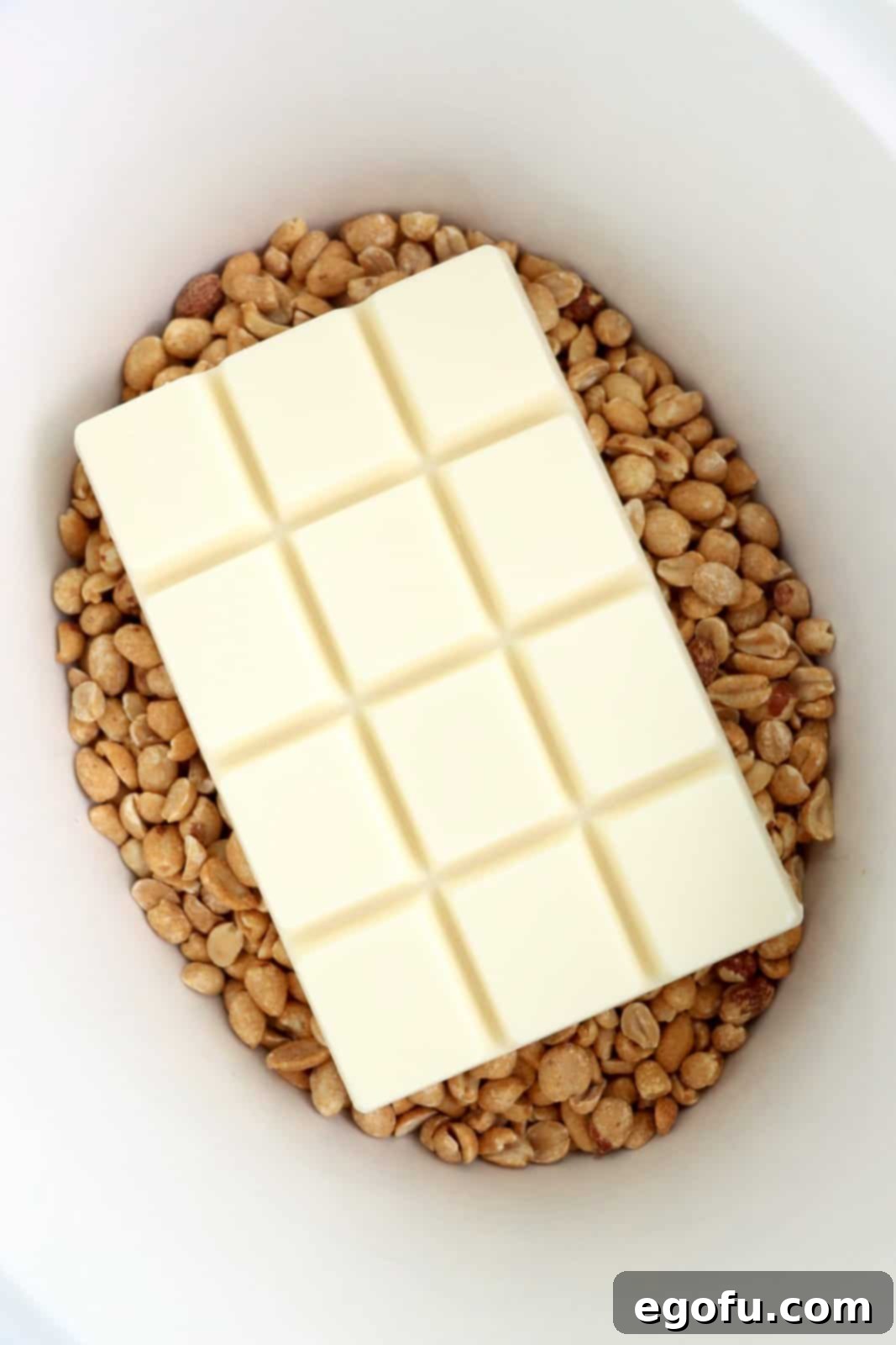 Effortless Slow Cooker Candies 5 A slow cooker insert with roasted peanuts on the bottom and almond bark on top.