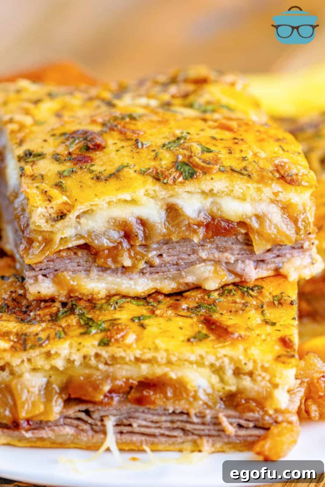 Close up looking at two french dip squares stacked on top of each other. The golden-brown crust and melted cheese are visible.