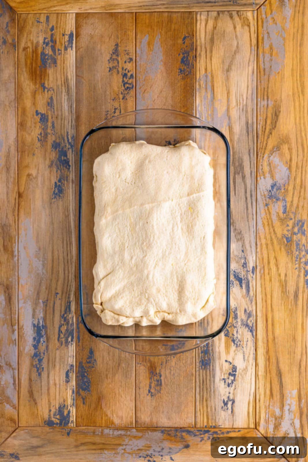 A baking dish with all layers complete, topped with the second crescent roll dough sheet, sealing in the roast beef, cheese, and onions.
