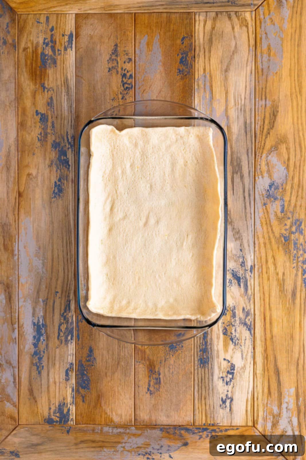 A baking dish with a smooth layer of crescent roll dough pressed into the bottom and extending slightly up the sides.