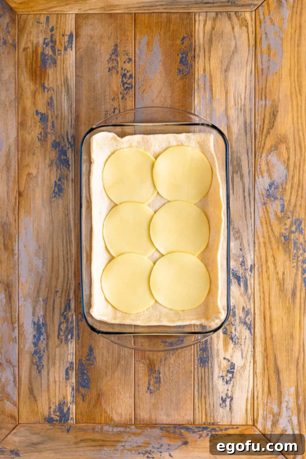 A baking dish with the crescent roll dough base covered uniformly with slices of provolone cheese.