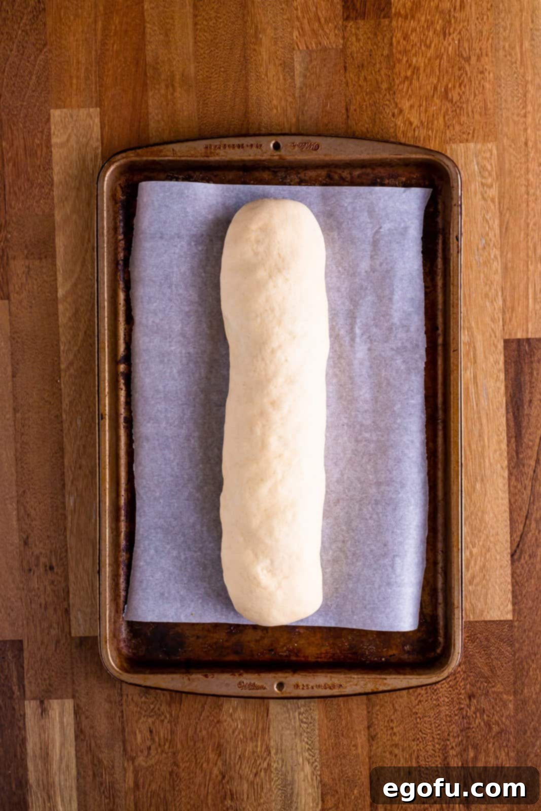 A parchment lined baking sheet with an uncooked sausage bread loaf, sealed and ready for the oven.