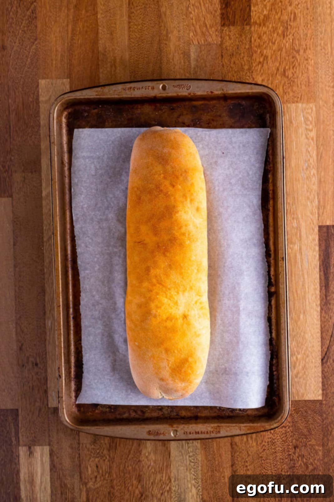 A fully baked sausage bread loaf on a parchment lined baking sheet, golden and inviting.