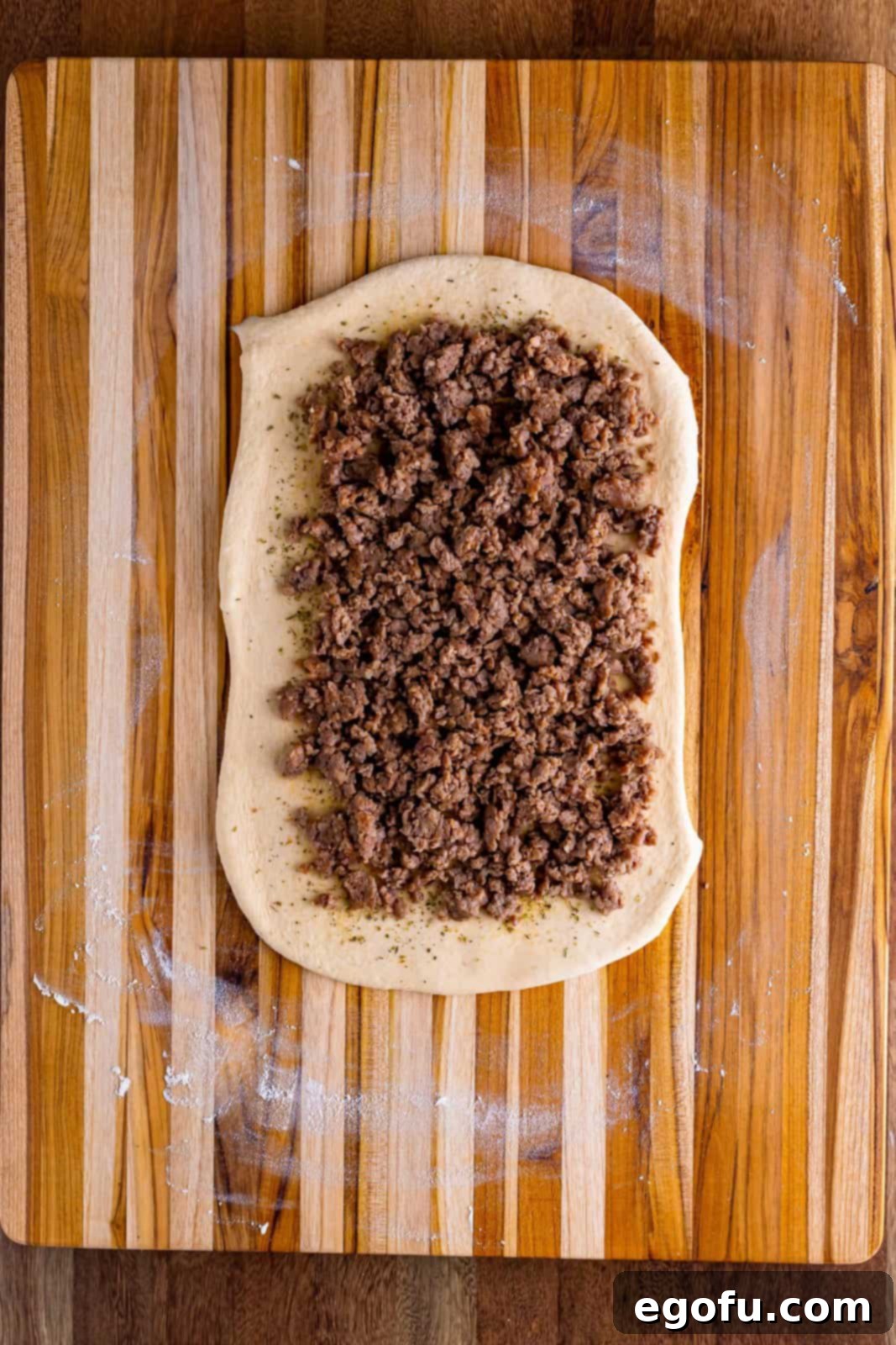Dough with cooked breakfast sausage spread, leaving clear borders.