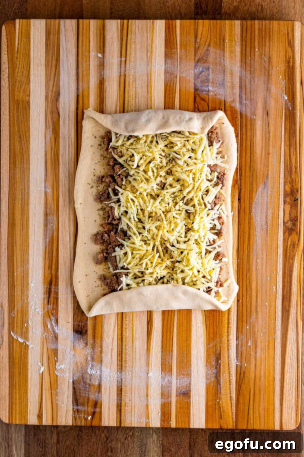 Bread dough rolled out with breakfast sausage, cheese, and spices with the top and bottom edges rolled in.
