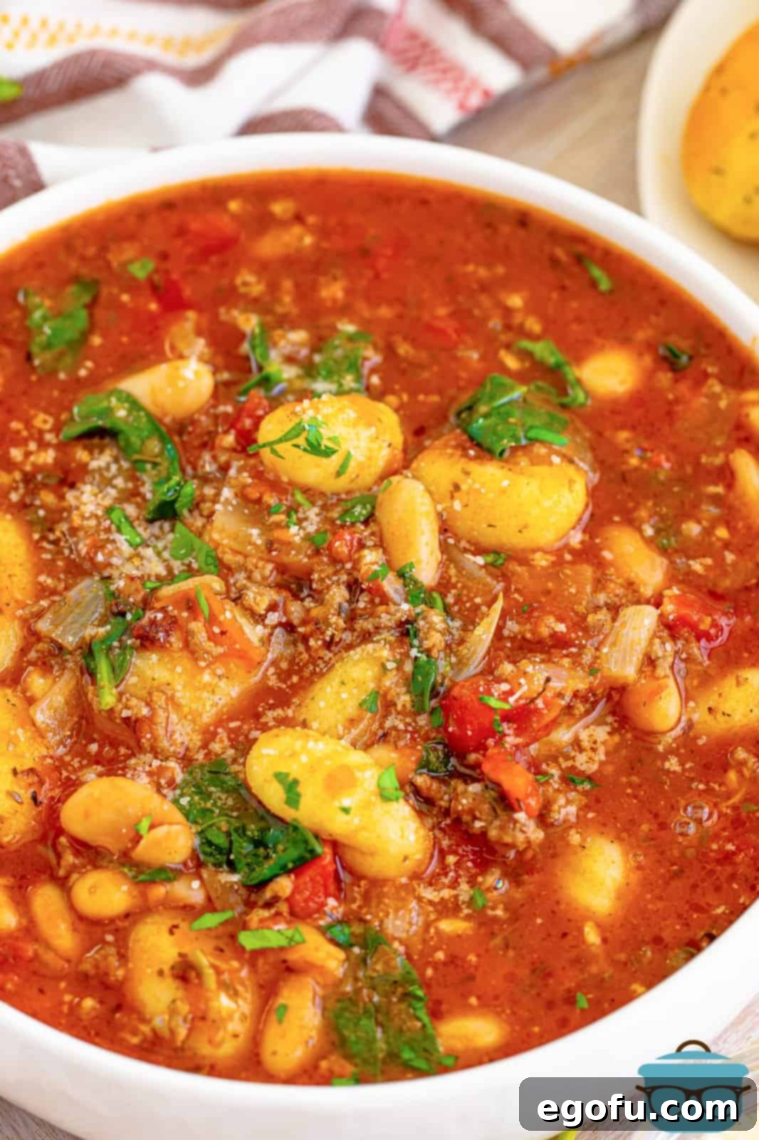 Close up looking at a white bowl of tomato based Italian Gnocchi Soup, garnished with fresh parsley.