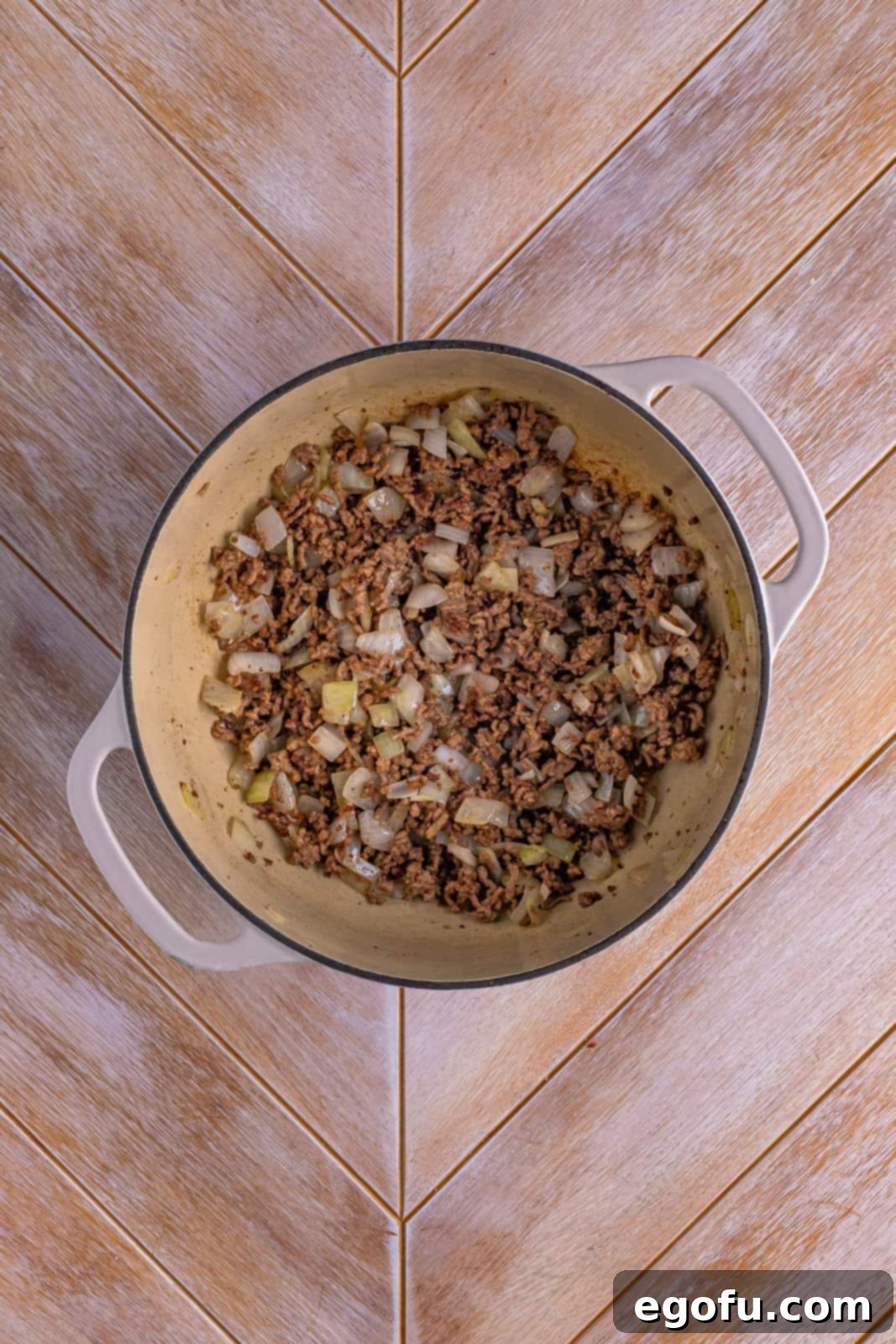 Dutch oven with cooked ground beef and softened diced onions.