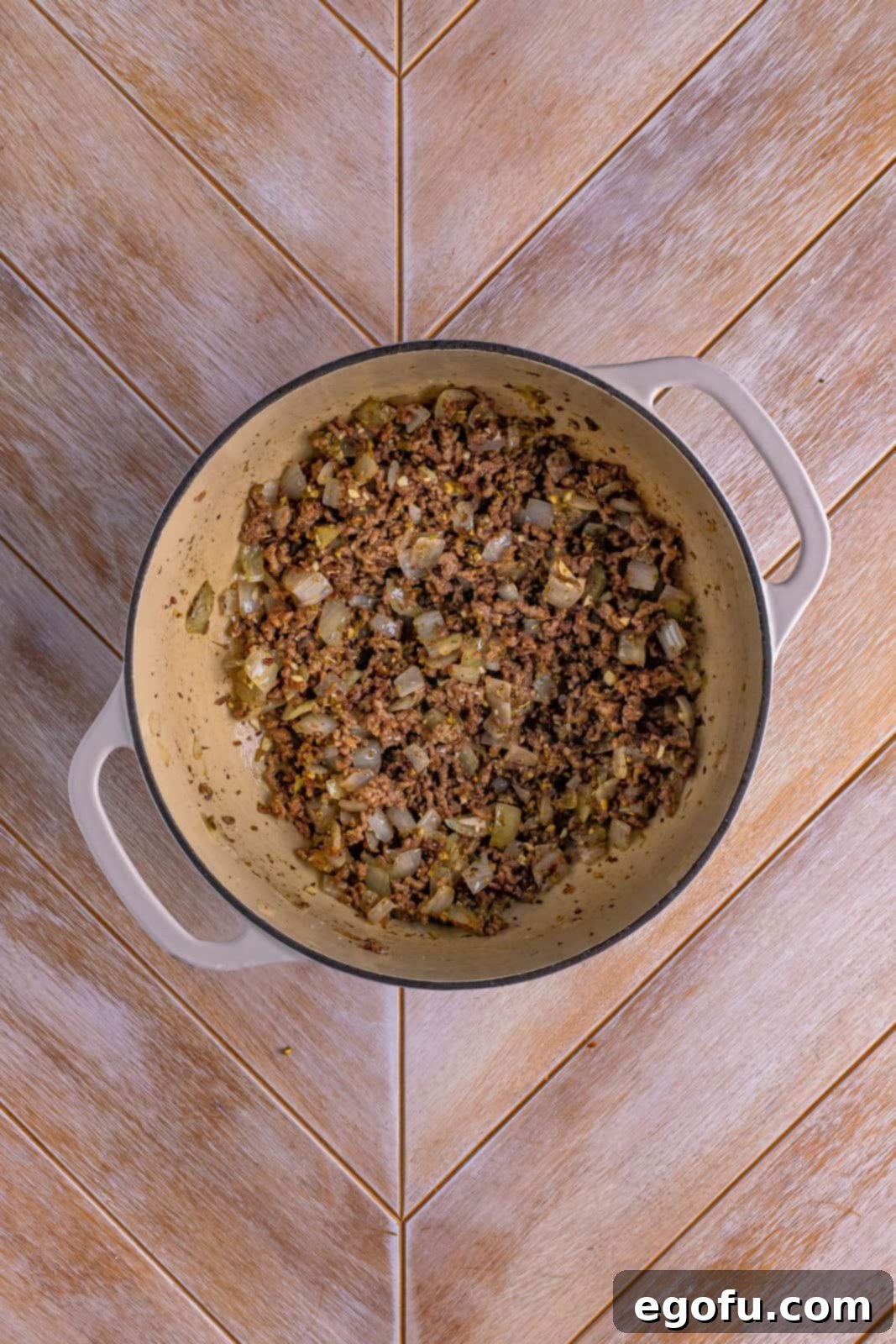 Dutch oven with cooked ground beef, diced onion, and aromatic spices and pesto mixed in.