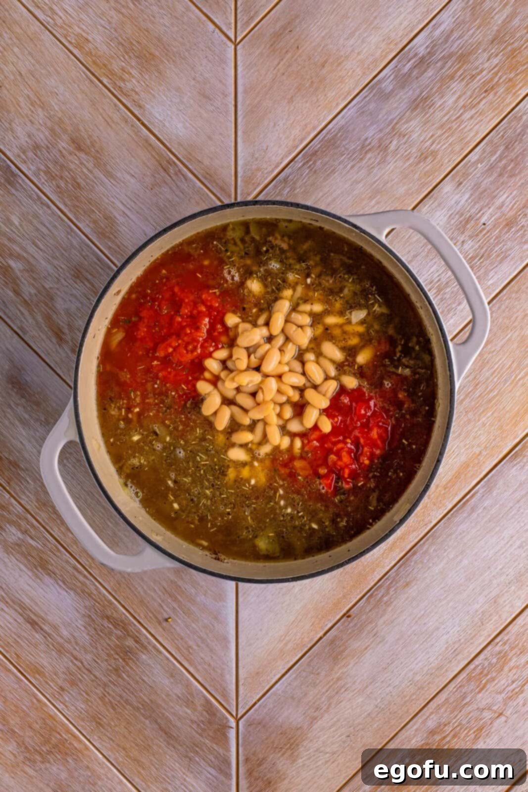 Dutch oven with ground beef, spices, chicken stock, pasta sauce, cannelini beans, and diced tomatoes, simmering gently.
