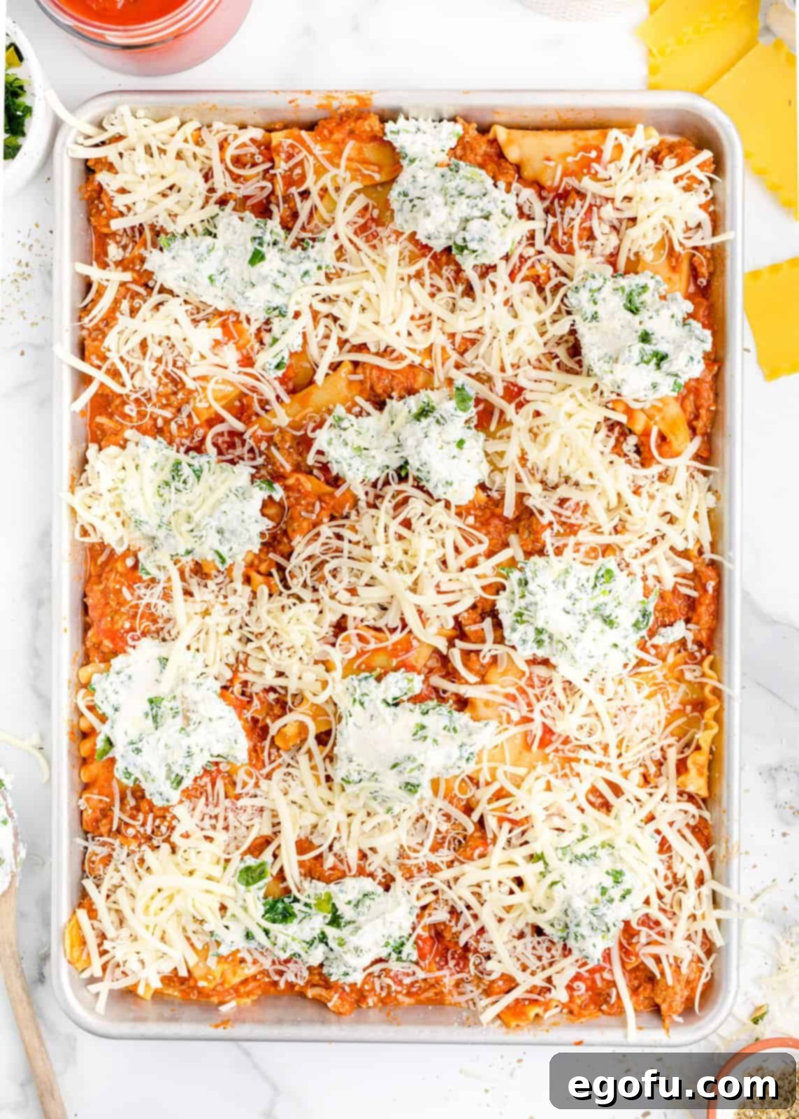 Close-up of a sheet pan lasagna, topped with grated Parmesan and mozzarella cheeses, glistening over the ricotta and meat sauce.