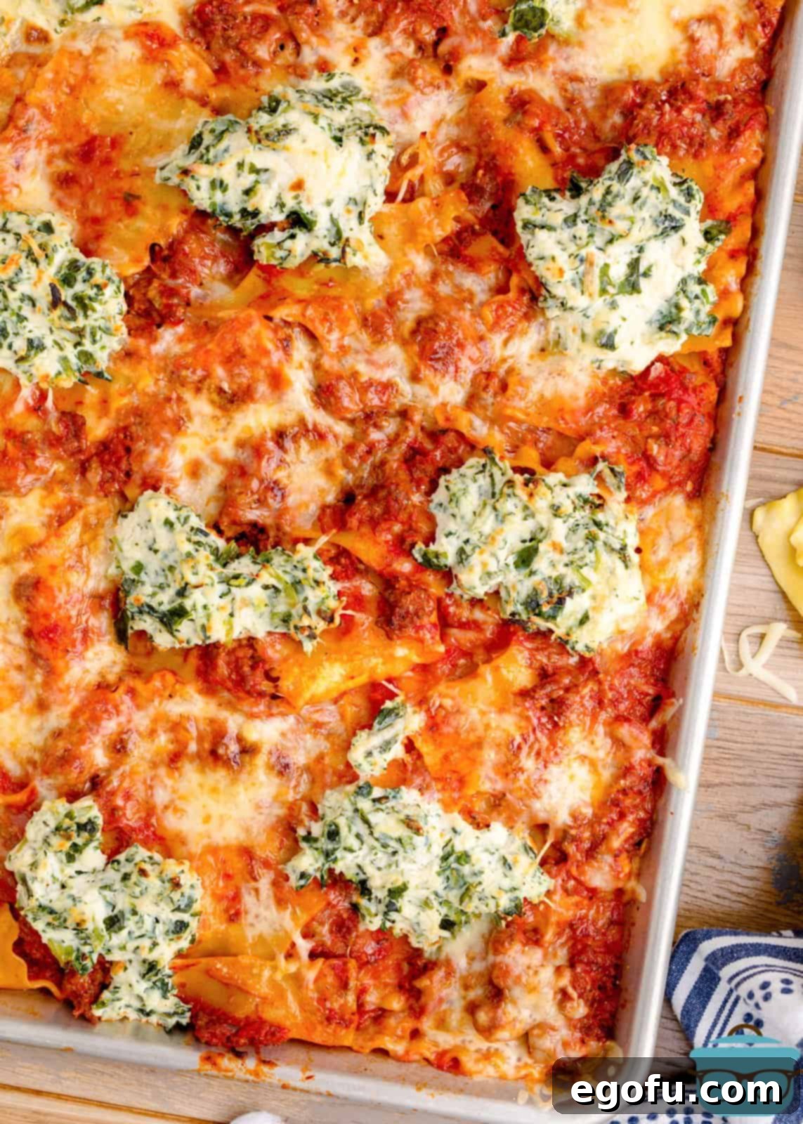 Close-up view of a corner of a perfectly baked Sheet Pan Lasagna, showing the golden, bubbly cheese and crispy edges.