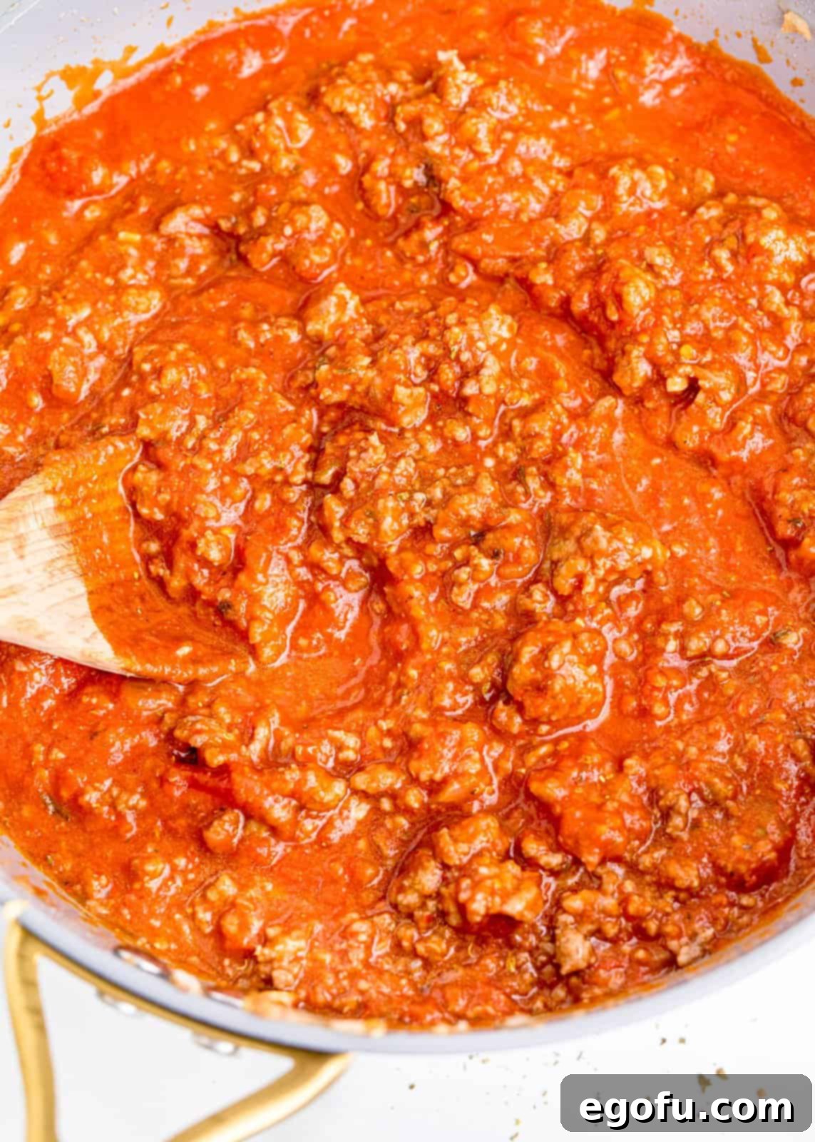 A skillet filled with a rich, simmering beef and marinara sauce, infused with Italian seasonings.