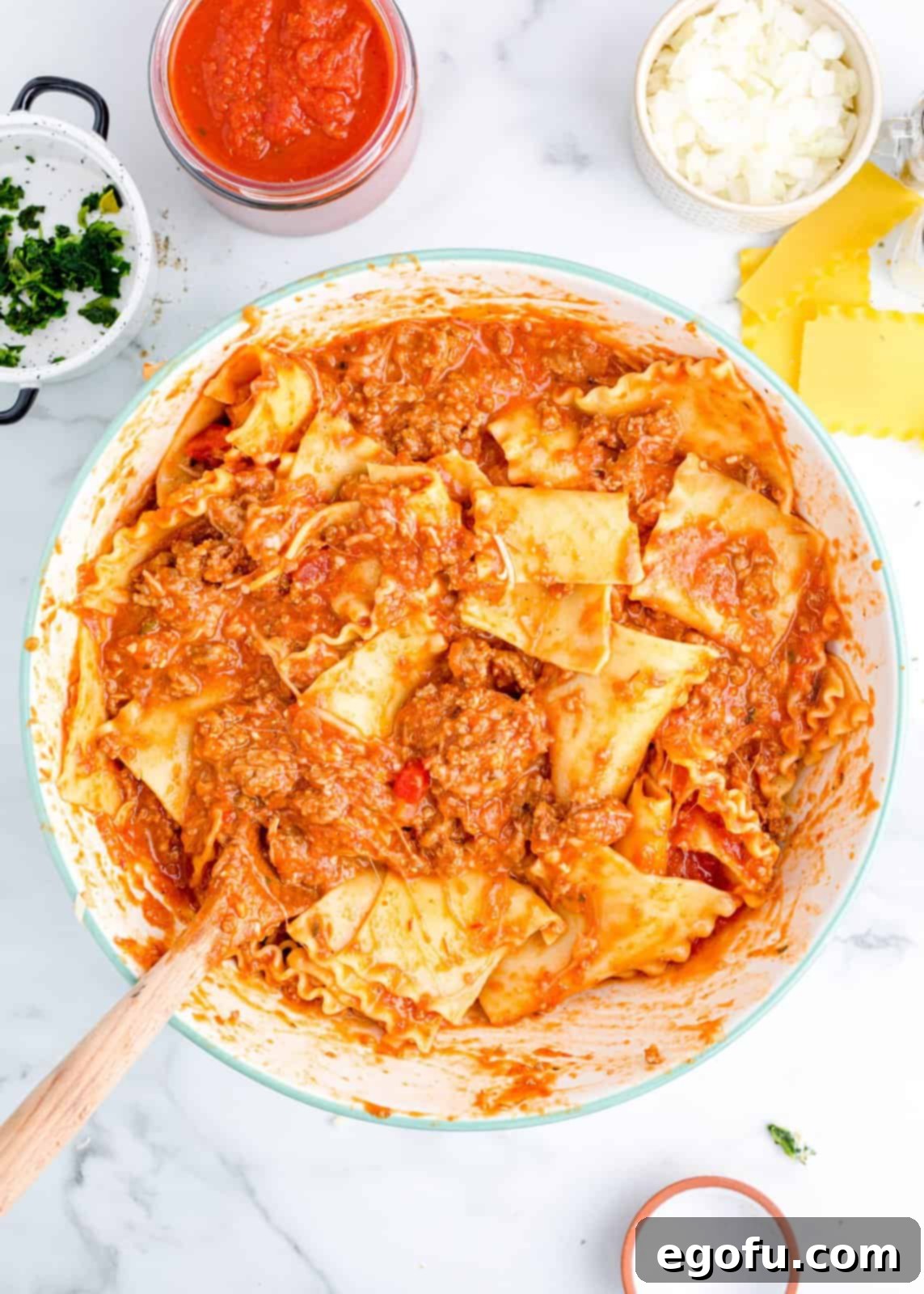 A large bowl filled with broken lasagna noodles, rich marinara meat sauce, and mixed cheeses, ready for the sheet pan.