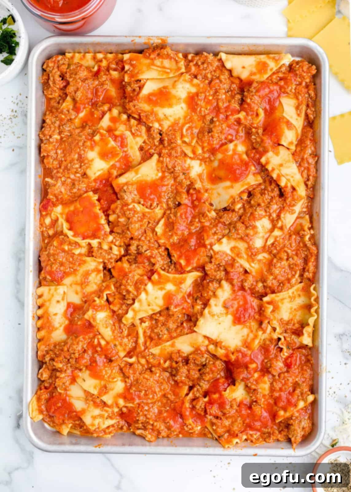 A sheet pan with evenly spread lasagna noodles, ground beef mixture, and marinara sauce.