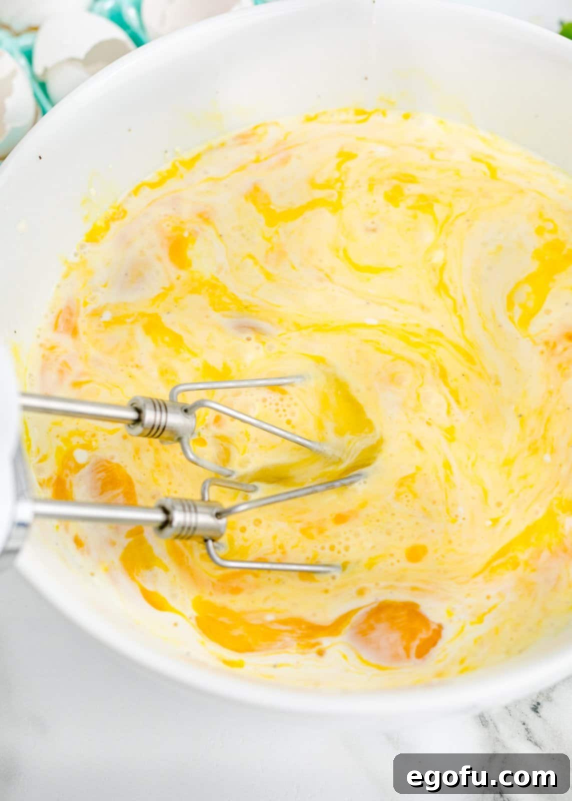 Baked Sheet Pan Eggs 5 A close-up view of a large mixing bowl where eggs are being expertly whisked with an electric hand mixer, creating a smooth, frothy, and perfectly combined mixture.