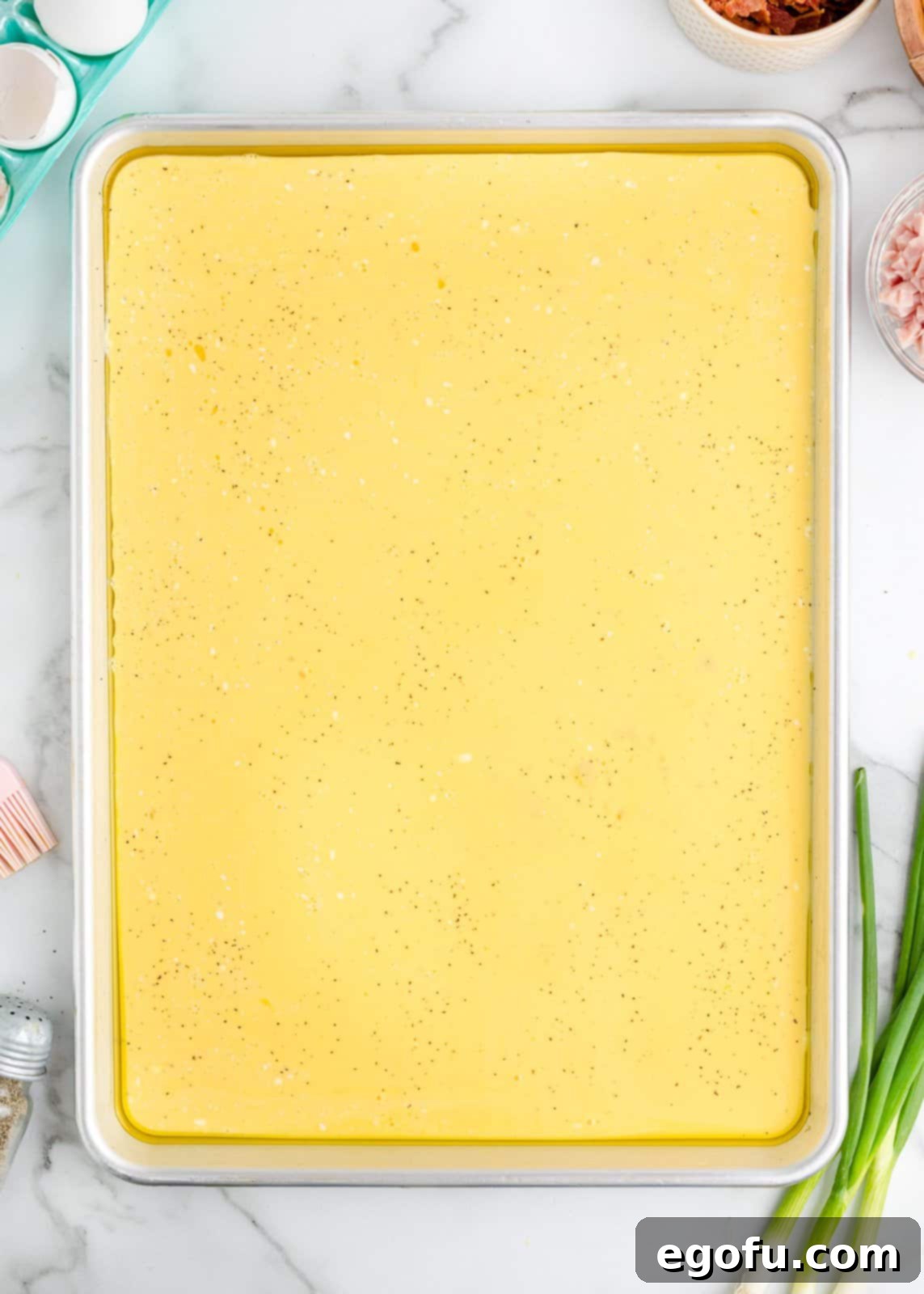 Baked Sheet Pan Eggs 6 A baking tray showcasing a perfectly smooth, bright yellow layer of beaten eggs, evenly spread and ready for toppings.