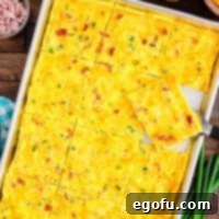 Baked Sheet Pan Eggs 10 A baking tray filled with cooked eggs, topped with crispy bacon, savory ham, fresh green onions, and melted cheese, with a generous portion already cut out and ready to serve.
