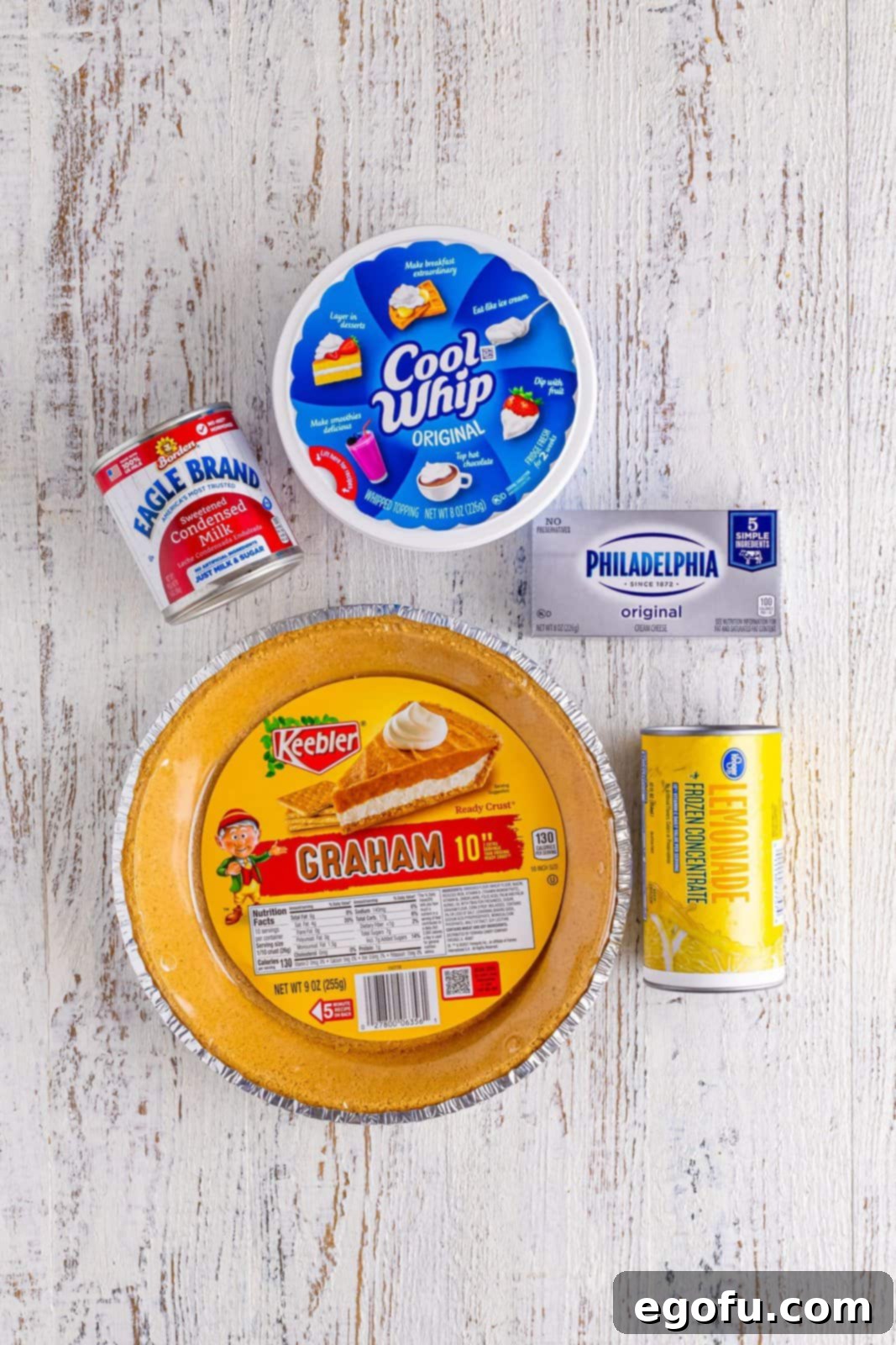 Individual ingredients for Lemonade Pie: Graham cracker crust, thawed lemonade concentrate, Cool Whip, softened cream cheese, and a can of sweetened condensed milk.