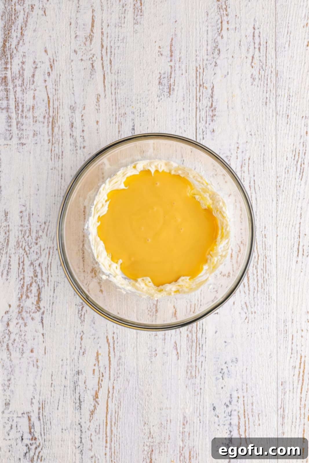 A mixing bowl containing a creamy mixture of condensed milk and cream cheese, with thawed lemonade concentrate freshly added.