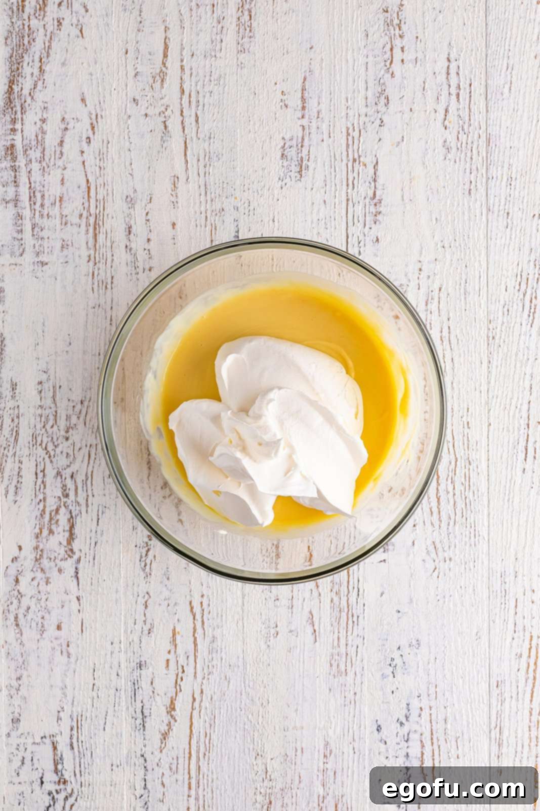 A bowl filled with a perfectly smooth lemonade pie filling, achieved by incorporating whipped topping until no streaks remain.